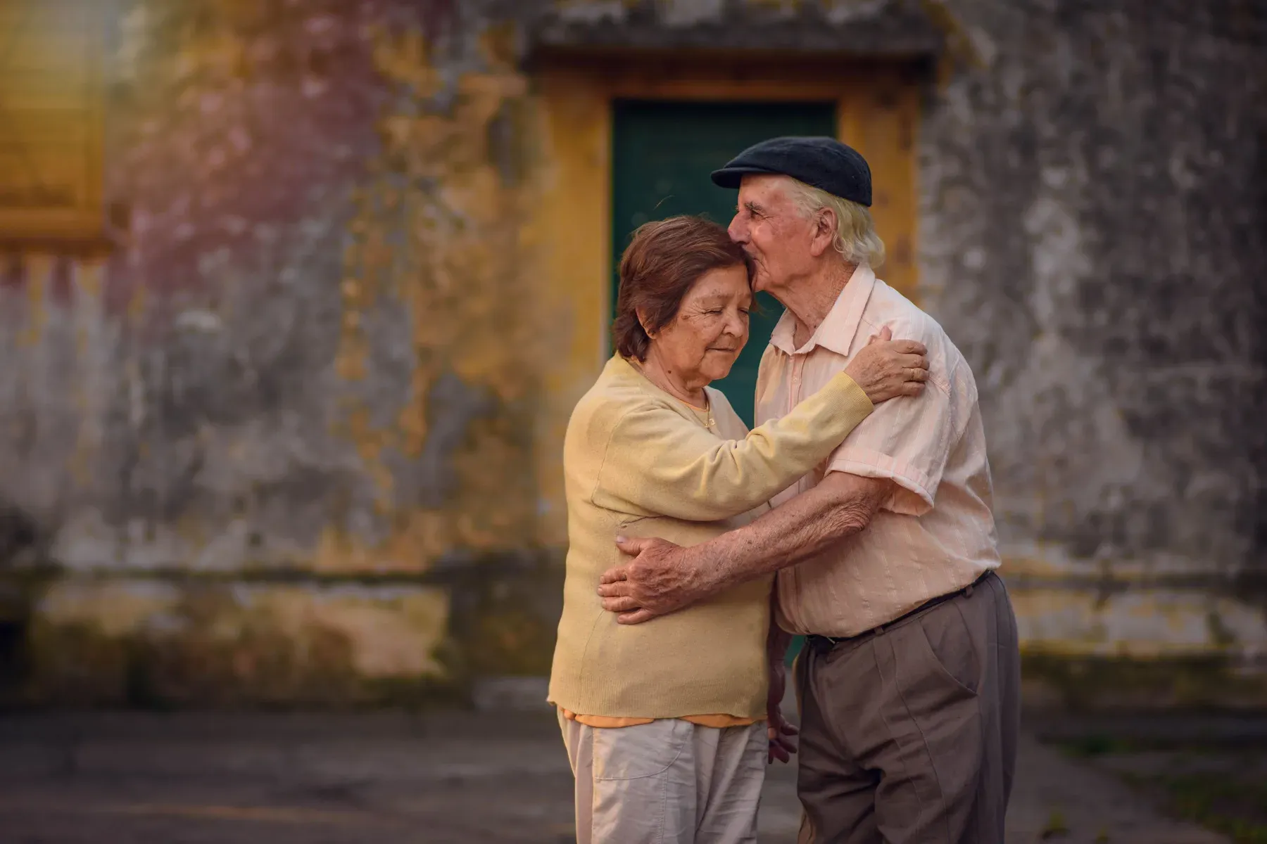An elderly couple embracing in a sunlit courtyard
