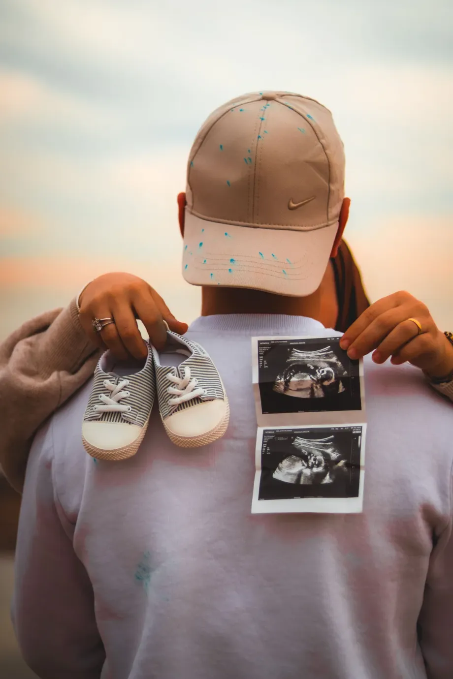 An expectant parent holding a pair of tiny shoes and two ultrasound scans