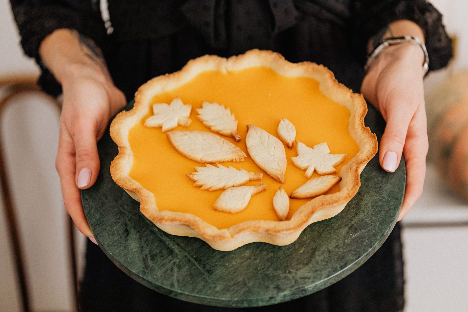 A pumpkin pie decorated with pastry leaves, held out on a plate