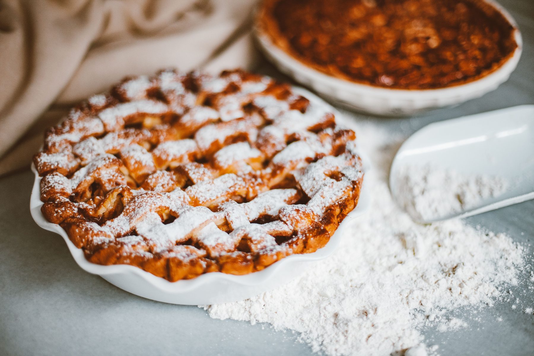 A lattice-top apple pie dusted with powdered sugar beside a scoop of flour
