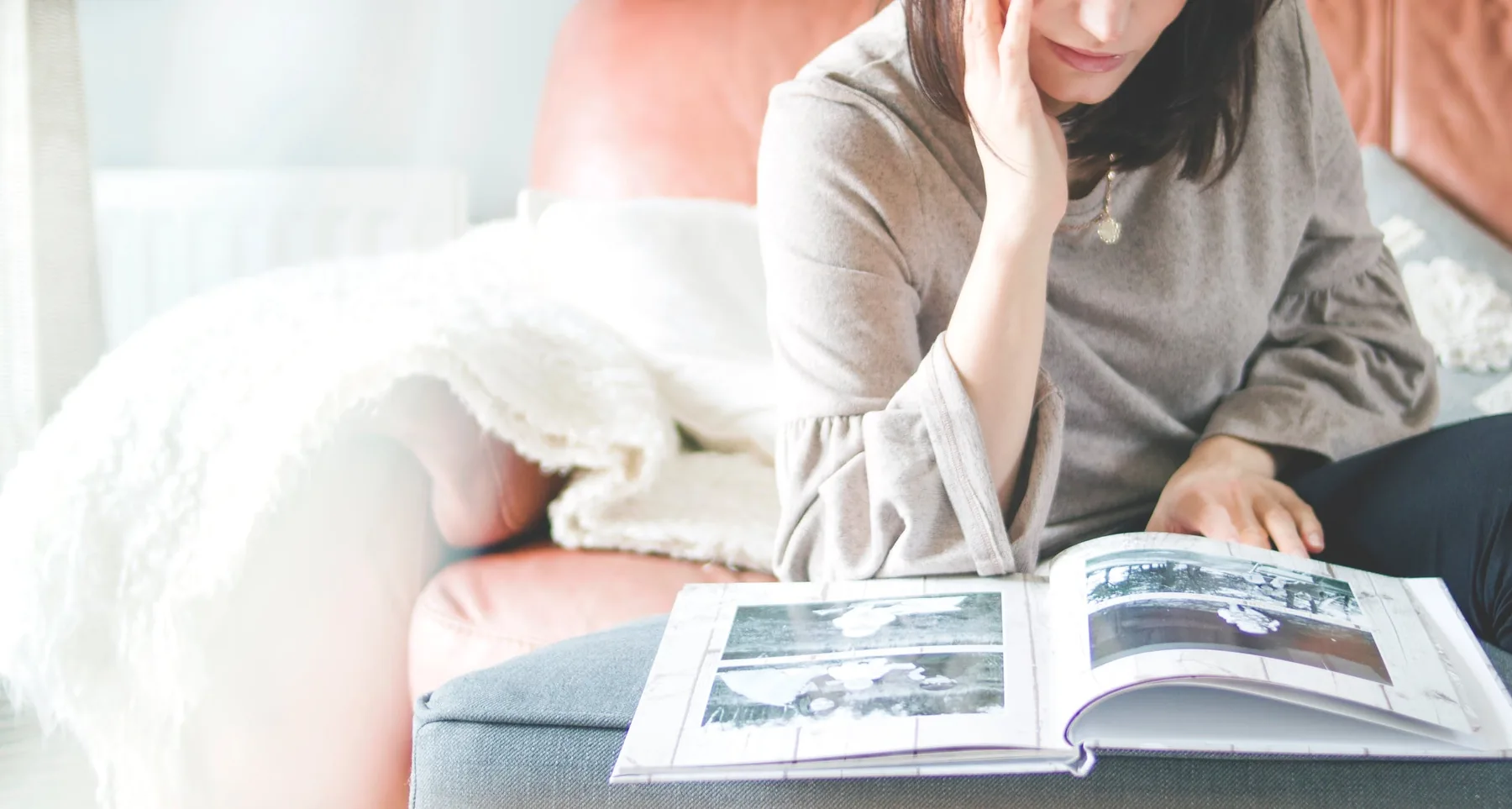 A young woman sitting on a bed looking through a printed photo book