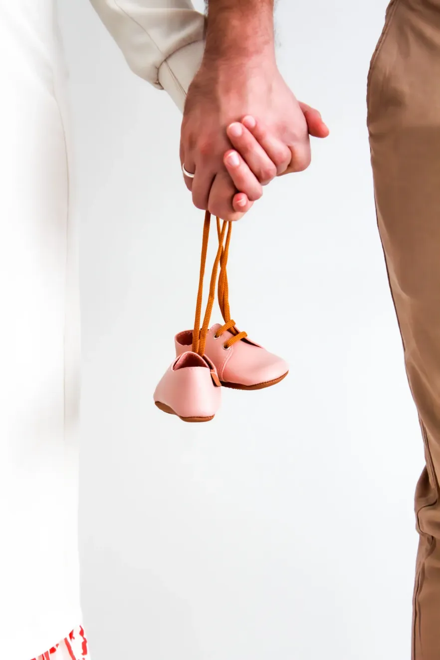 An adult hand holding a pair of tiny shoes by their laces