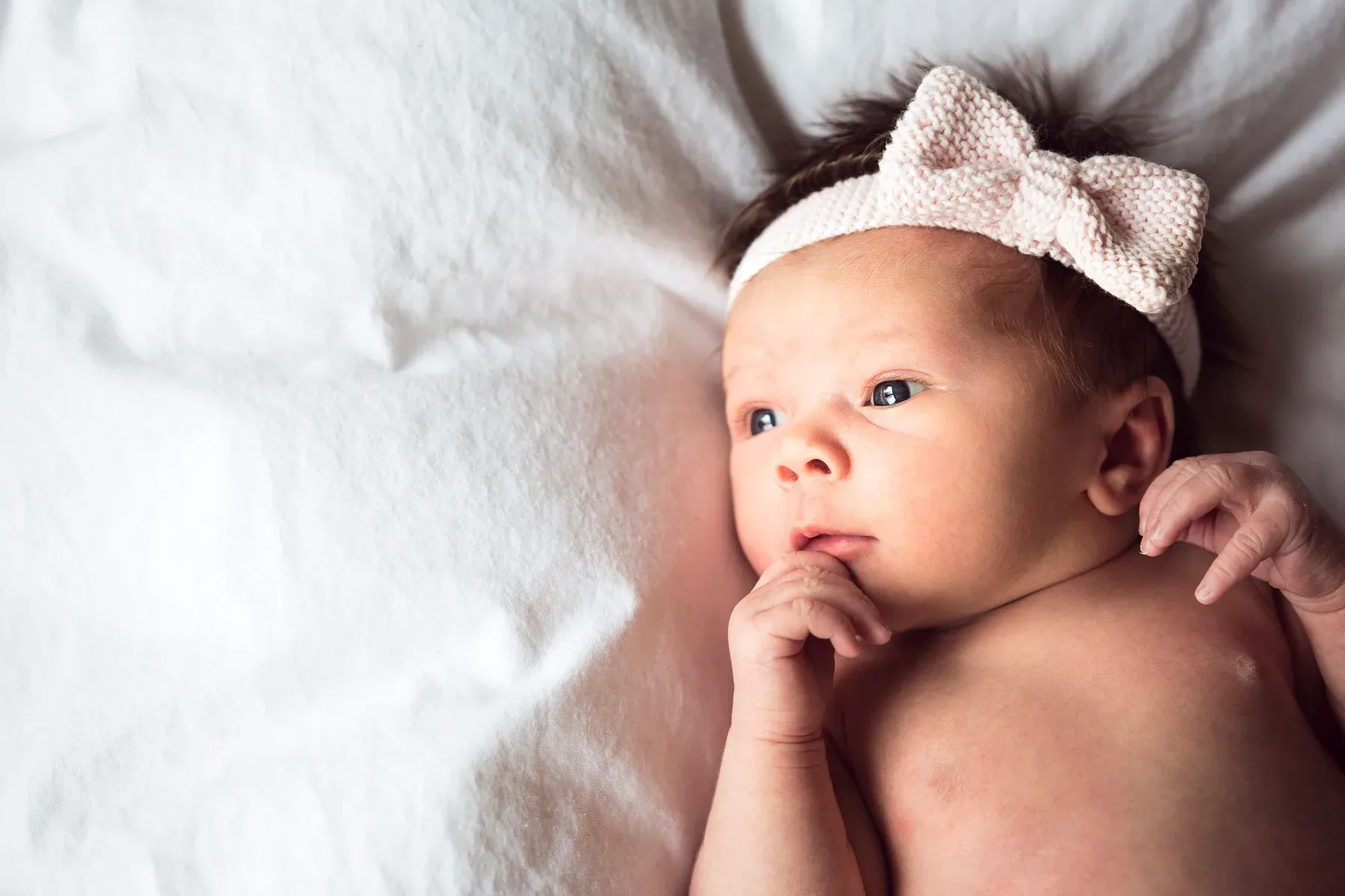 A newborn in a bow headband lying on a white blanket