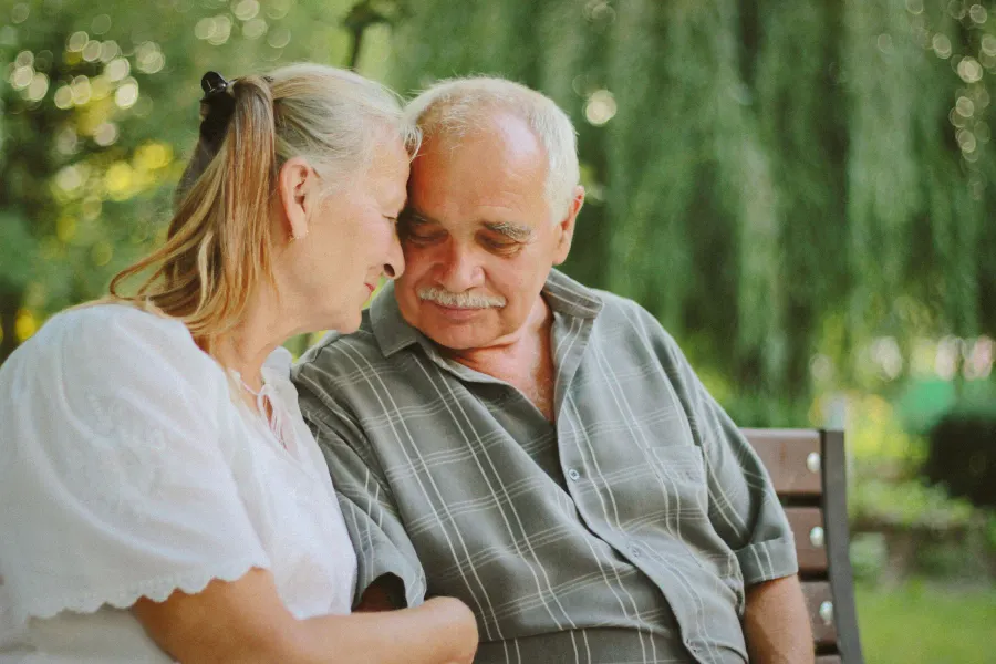 An older couple sitting close on a park bench