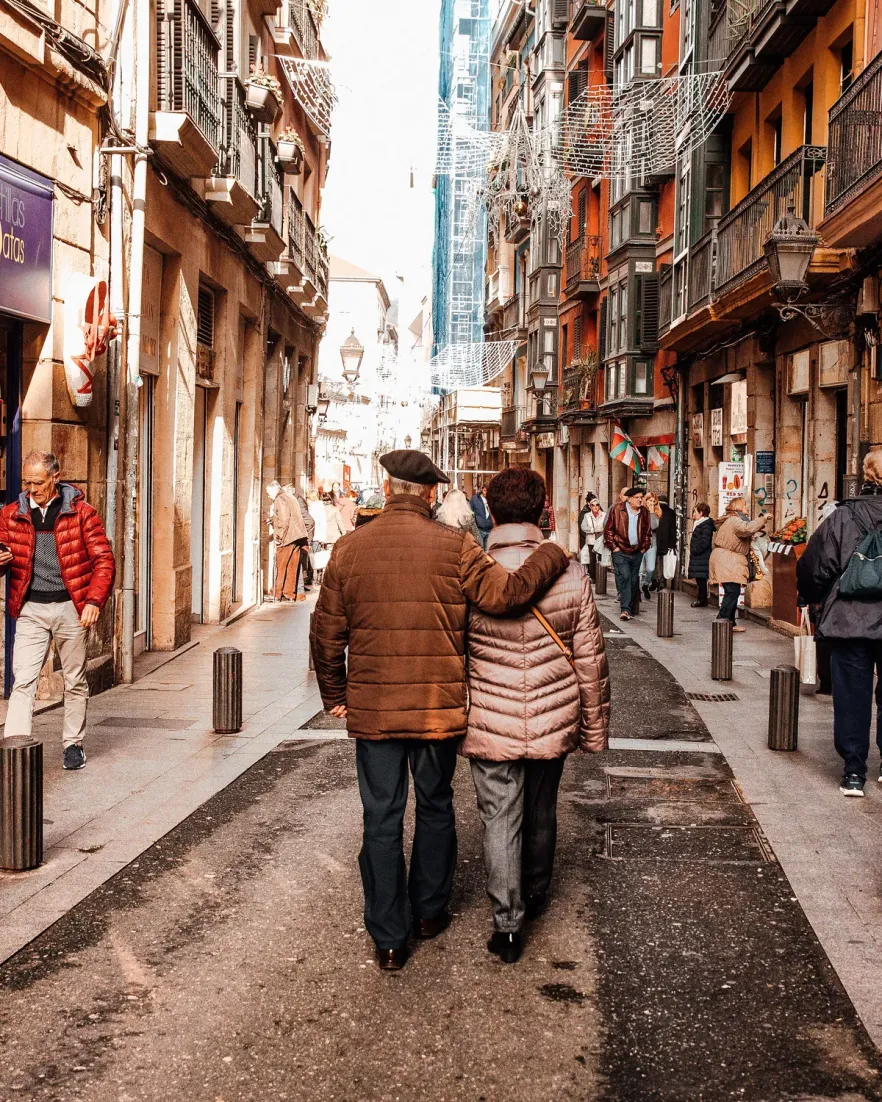 An older couple walking arm in arm down a narrow city street in winter coats