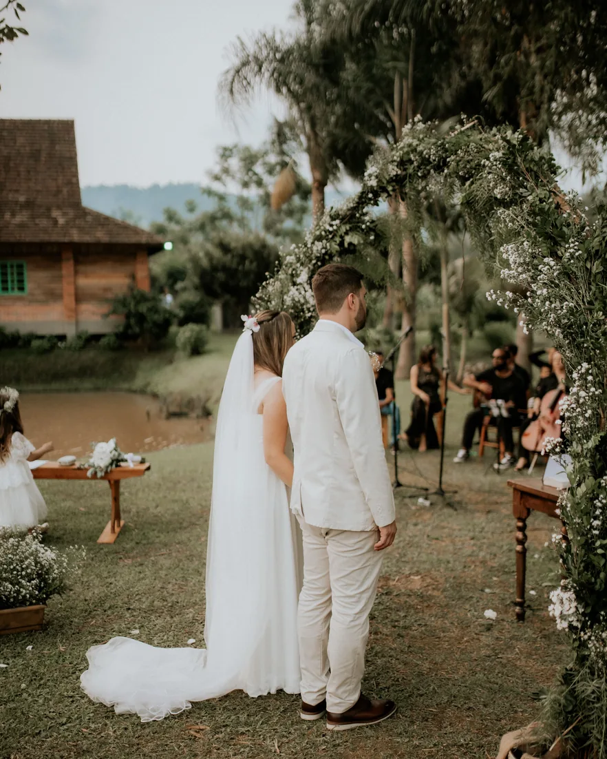 A couple standing under a greenery arch at an outdoor ceremony
