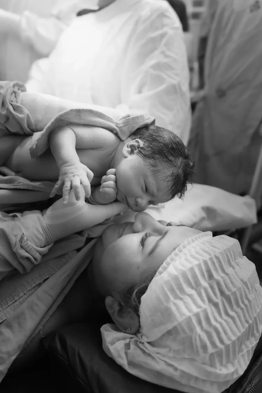 A black and white photograph of a parent leaning over their sleeping newborn