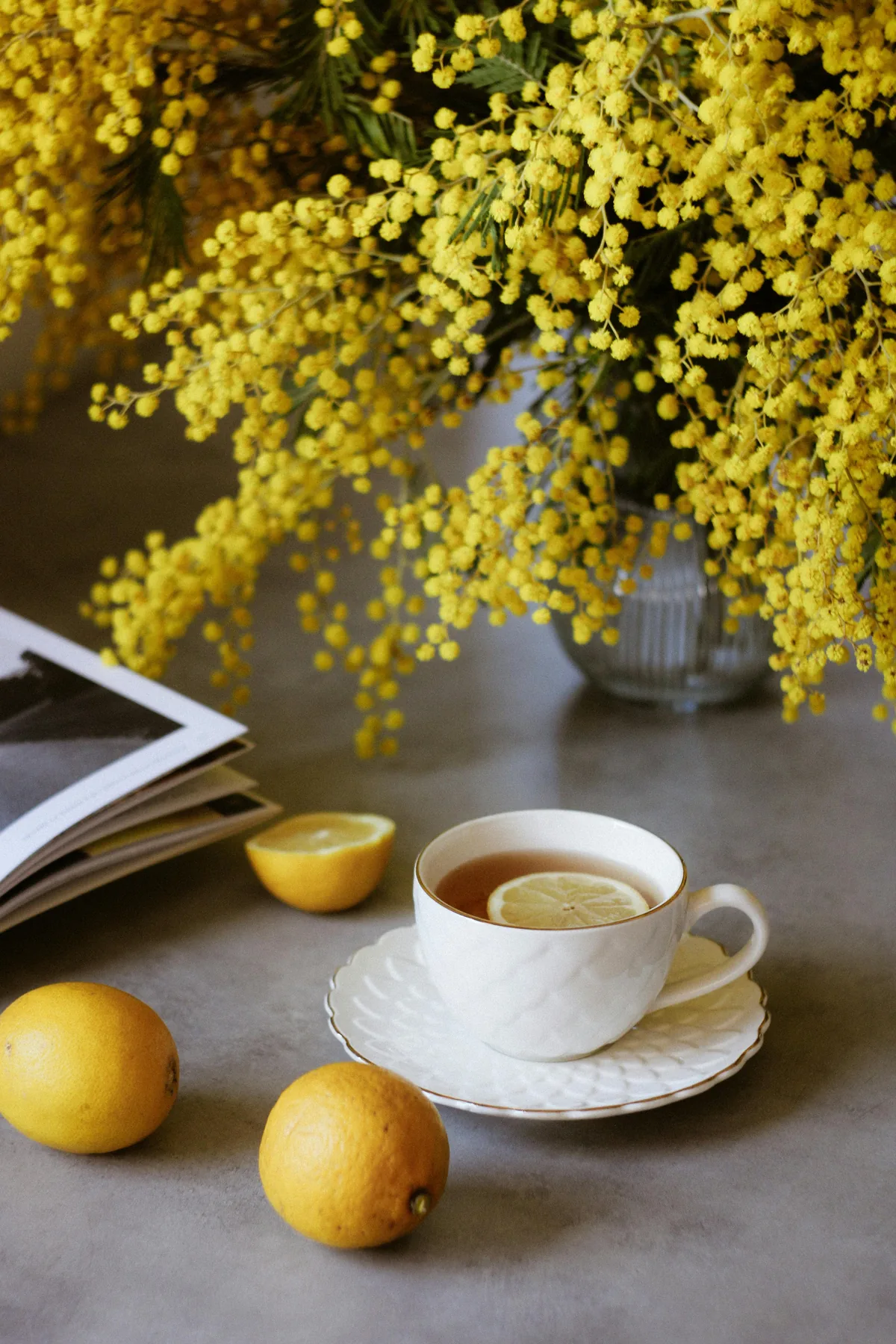 A vase of yellow mimosa beside a cup of tea on a table
