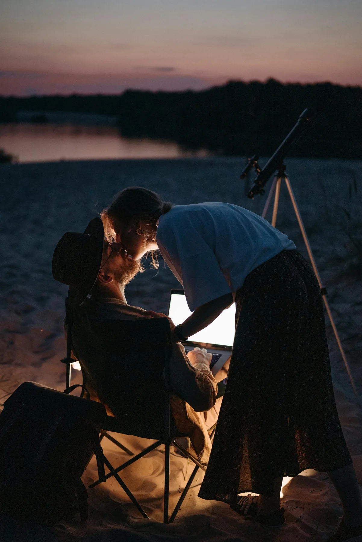 A couple sitting close together at dusk beside a lake