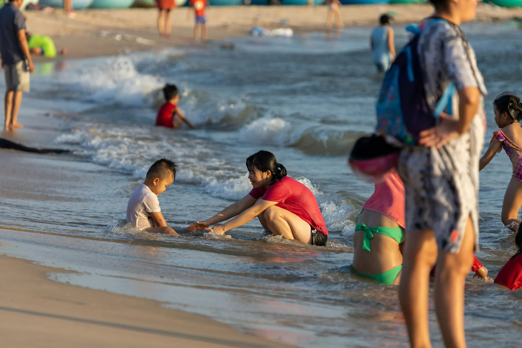 An extended family with children playing together at the edge of the water on a beach
