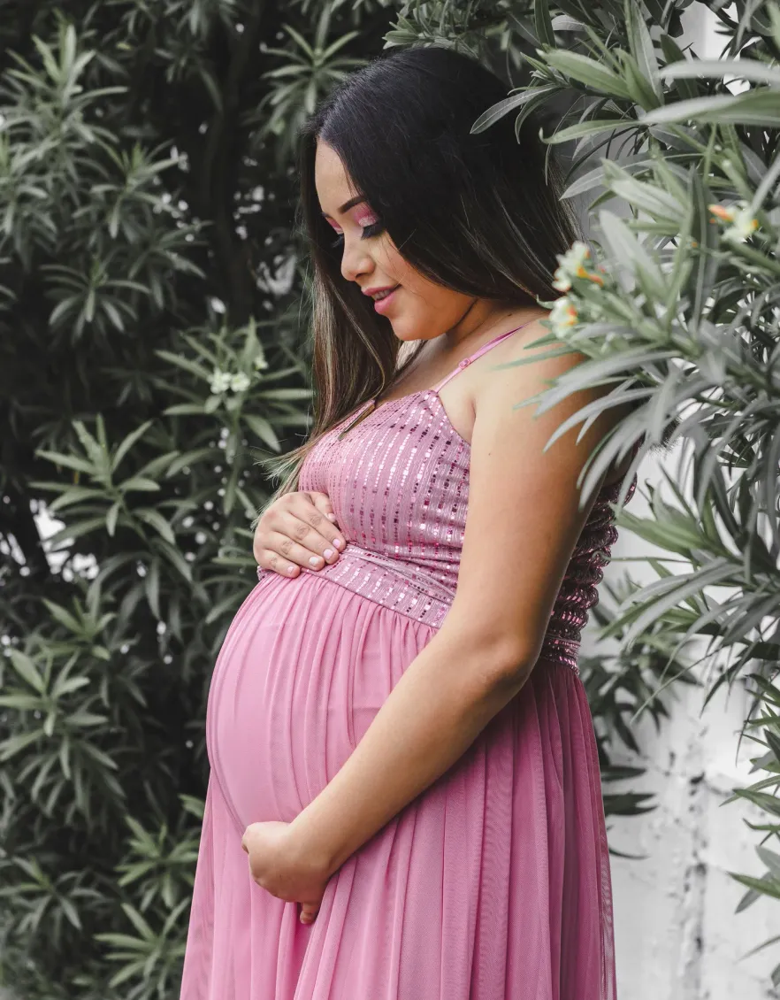 A pregnant woman standing outdoors with her hands resting on her bump
