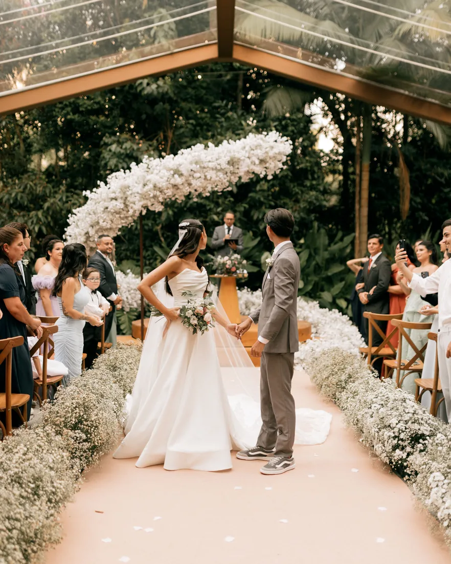 A couple at the altar during an outdoor ceremony, guests seated along both sides of the aisle